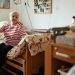 Elderly woman in striped shirt sits comfortably in her retirement home bedroom, surrounded by personal items.